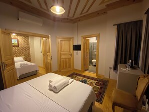 Habitación de hotel con cama, una silla, escritorio, televisión y baño visible a través de una puerta abierta.