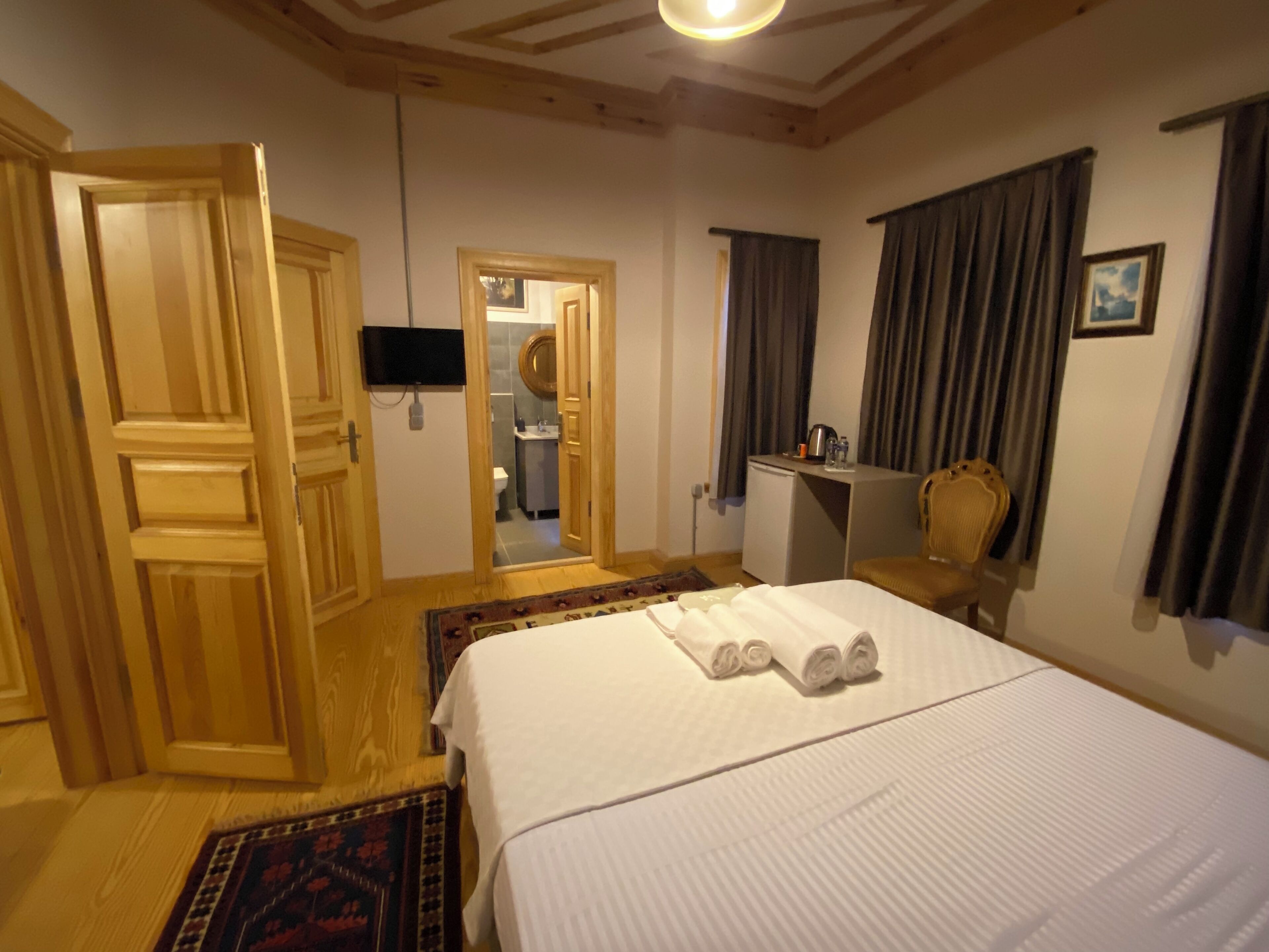 A hotel room with a bed, a desk, a chair, a television, and a bathroom visible through an open door.