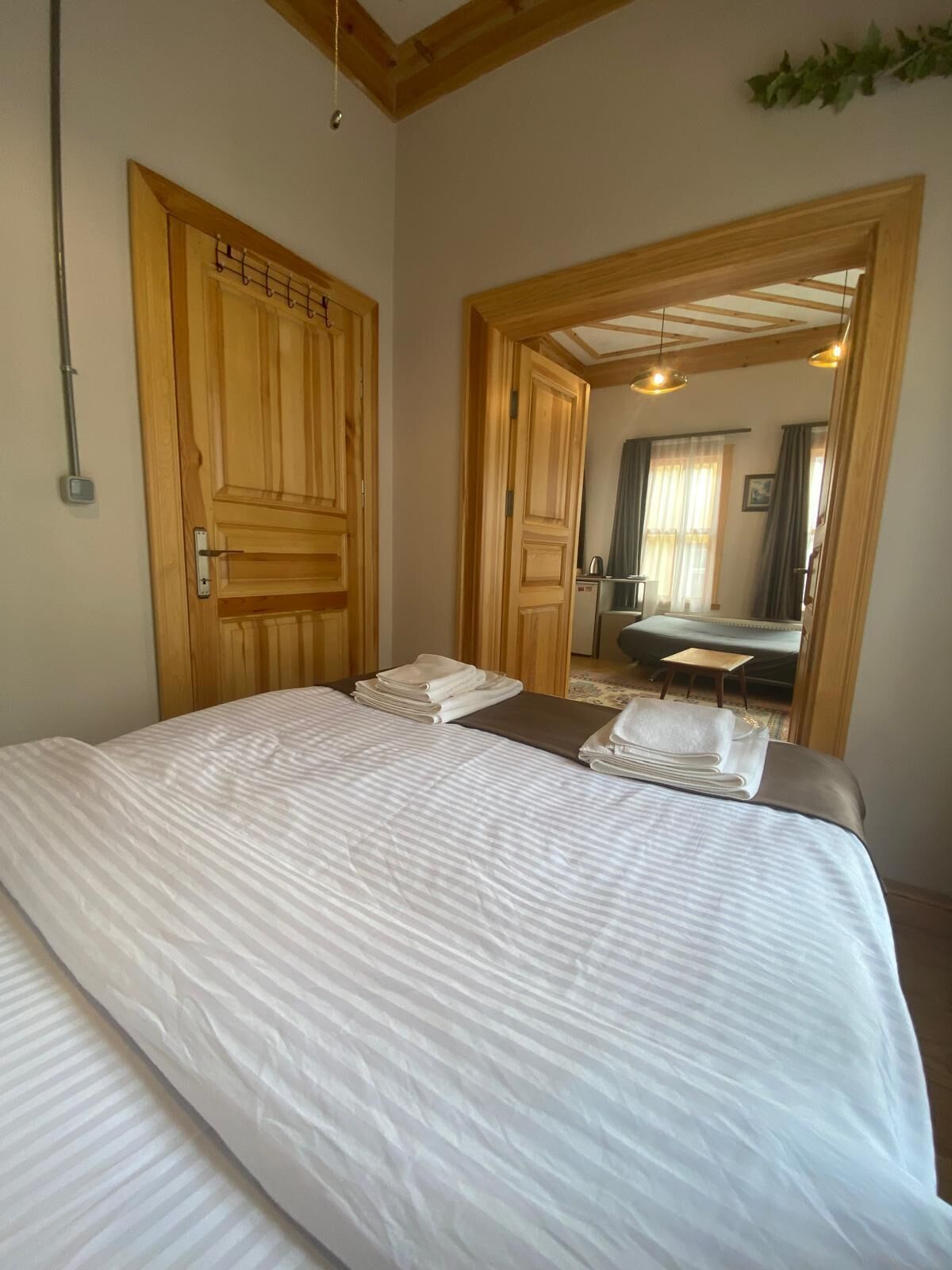 A bedroom with a large bed, wooden doors, and a view into another room with a desk and chair.