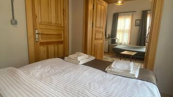 A bedroom with a large bed, wooden doors, and a view into another room with a desk and chair.