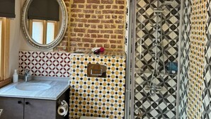 A bathroom with a brick wall, a mirror, a sink, a toilet, and a shower with patterned tiles. - HanFlats Hotel (Istanbul)