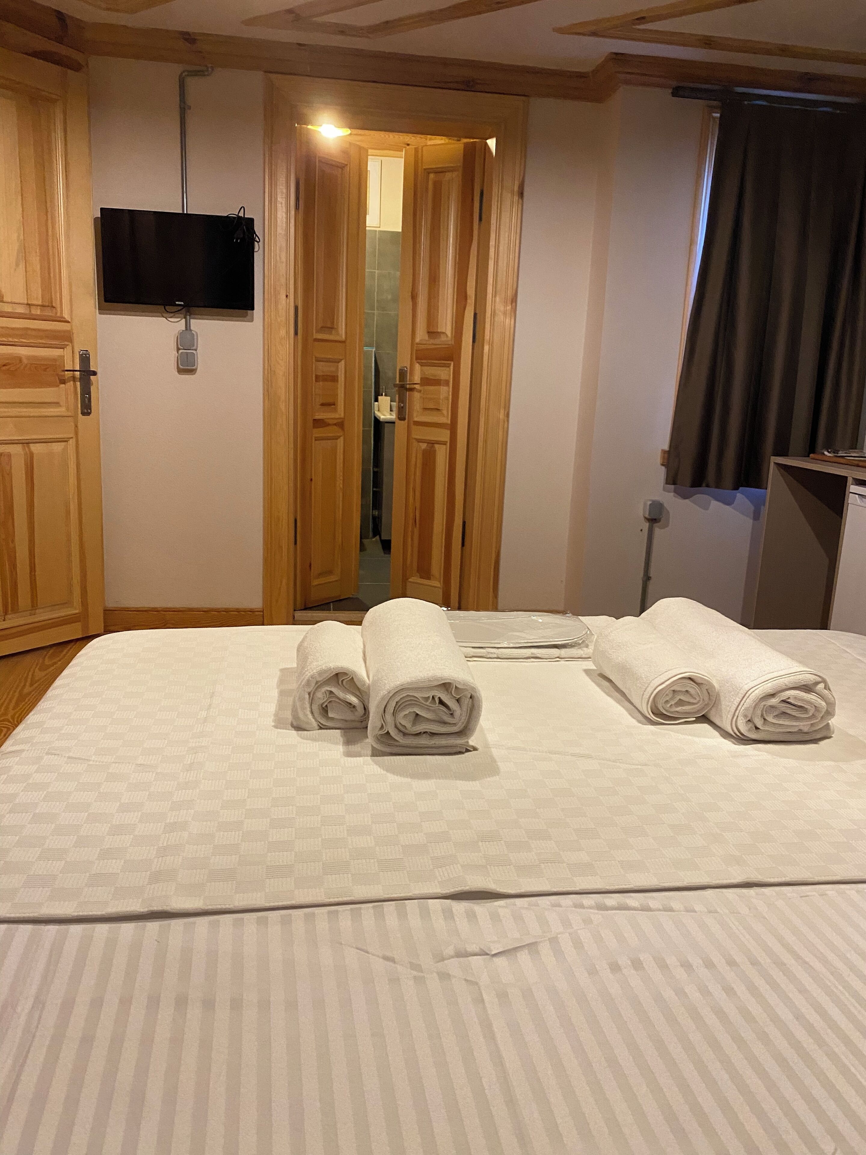 A hotel room with a bed, a TV mounted on the wall, wooden doors, and a bathroom visible through an open door.