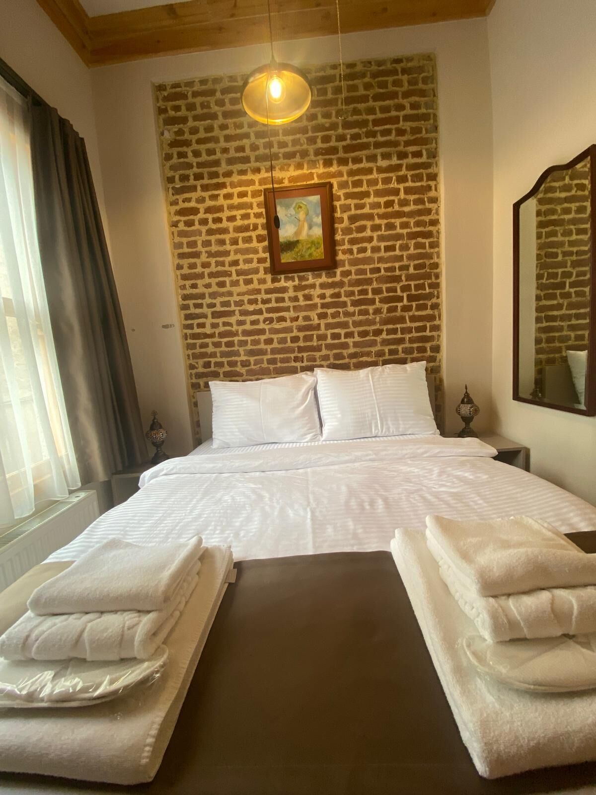 A hotel room with a brick wall, a bed with white linens, and a hanging light fixture.