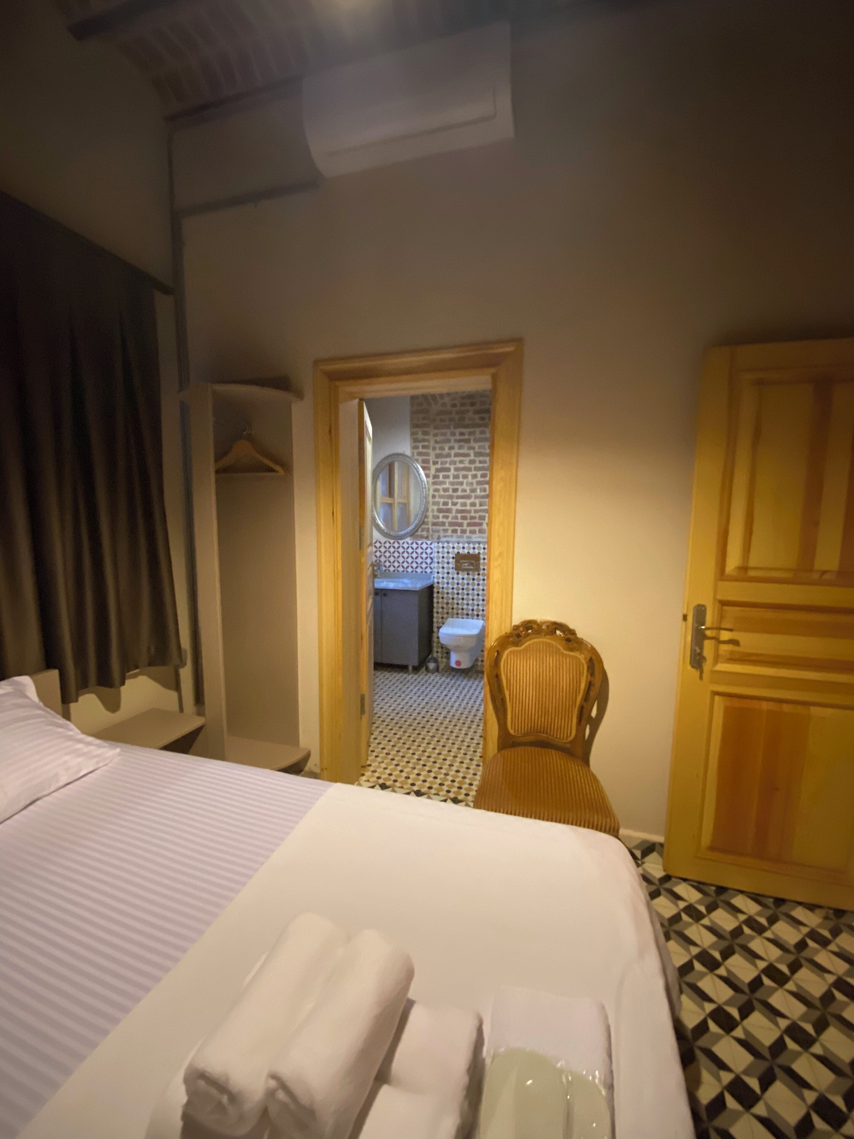 Une chambre d’hôtel avec un lit, une chaise, une porte en bois et une salle de bain visible à travers une porte ouverte.