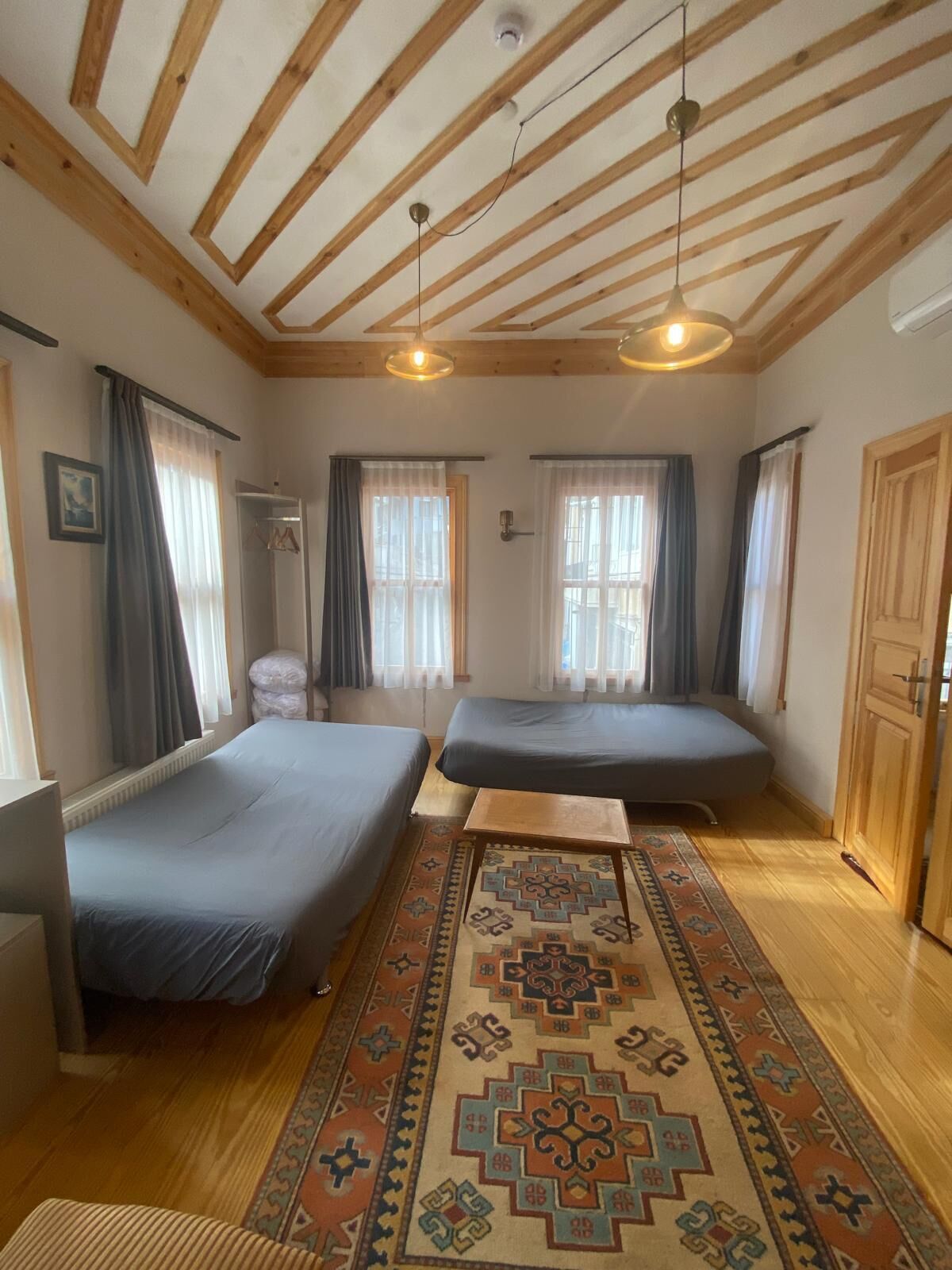Una habitación con dos camas, techo de madera, alfombra estampada y una ventana con cortinas.