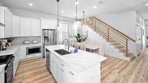 Une cuisine moderne avec des meubles blancs, un îlot central, des appareils électroménagers en acier inoxydable et un escalier en bois.