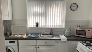 A kitchen with white cabinets, a sink, a microwave, a stove, and a clock on the wall. - Posh Pad Woolton Village (Liverpool)