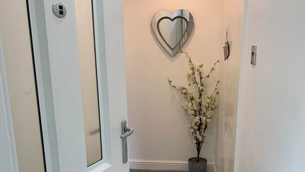 A hallway with a white door, a heart-shaped mirror on the wall, and a potted plant. - Posh Pad Woolton Village (Liverpool)