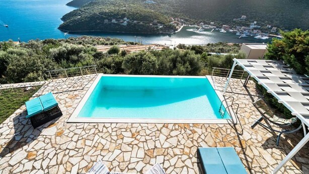 A swimming pool with stone tiles, surrounded by lounge chairs and a view of a coastal town. - Villa Sapfo in Lefkada (Lefkada)