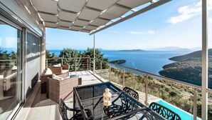 A balcony with wicker furniture, a glass door, and a view of the sea and hills. - Villa Sapfo in Lefkada (Lefkada)