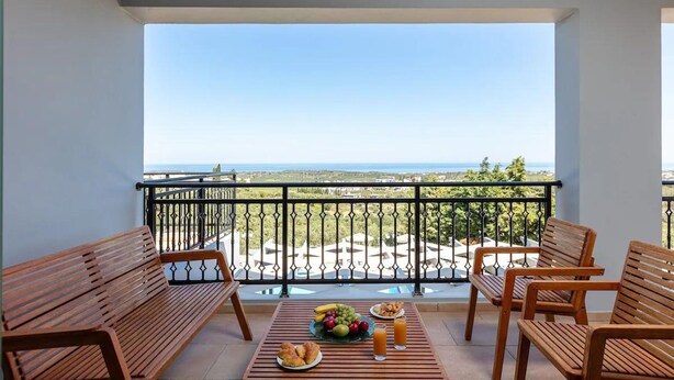 Ein Balkon mit Holzmöbeln, einem Tisch mit Früchten und Getränken sowie Blick aufs Meer.