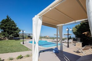 A covered outdoor area with a pool, lounge chairs, and umbrellas. - Villa Kyveli in Rethymno (Rethymno)