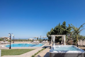 A swimming pool with lounge chairs and a hot tub, surrounded by trees and umbrellas. - Villa Kyveli in Rethymno (Rethymno)