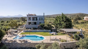 Ein modernes, zweistöckiges Haus mit Swimmingpool, Sitzgelegenheiten im Freien und Blick auf die umliegende Landschaft.
