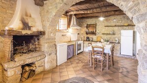 A rustic kitchen with stone walls, a fireplace, a dining table, and basic kitchen appliances. - Baciola in Ortignano Raggiolo (Ortignano Raggiolo)