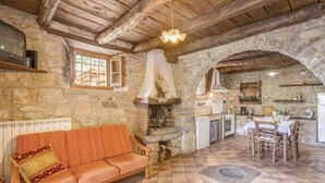A rustic interior with a stone fireplace, wooden beams, a sofa, a dining table, and a kitchen area. - Baciola in Ortignano Raggiolo (Ortignano Raggiolo)