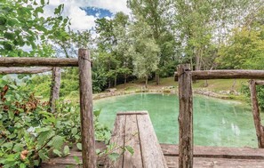 Eine rustikale Holzterrasse mit Blick auf ein klares, grünes Schwimmbecken, umgeben von üppigem Grün.