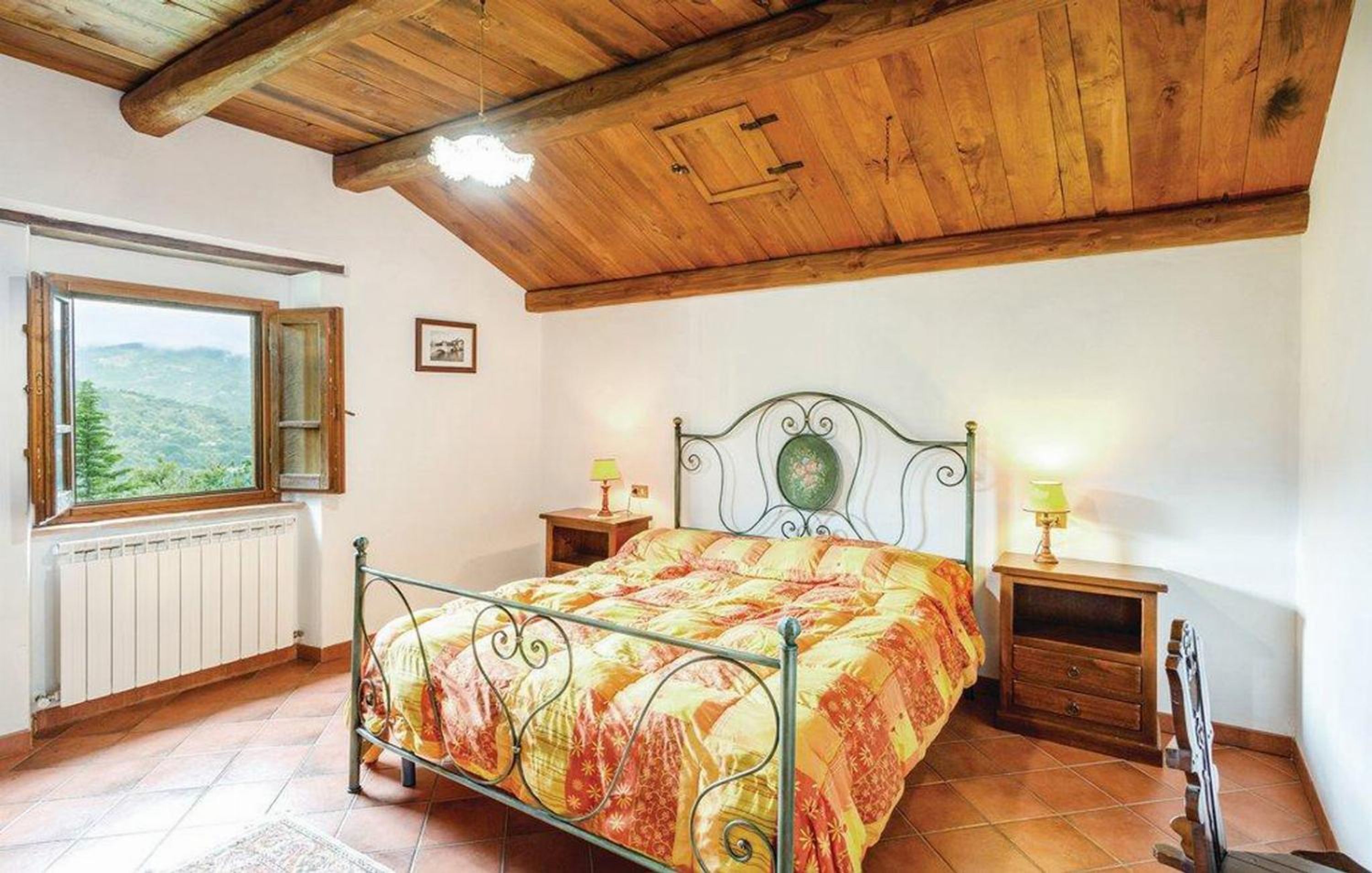 A bedroom with a bed, wooden ceiling, a window with a view, and two bedside tables with lamps.