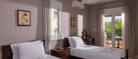 Hotelkamer met twee bedden, een raam met gordijnen, een airconditioning en uitzicht op groen.