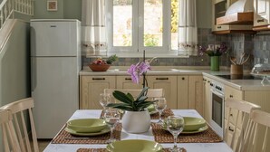 Uma cozinha com uma mesa de jantar posta para dois, geladeira e uma janela com cortinas.