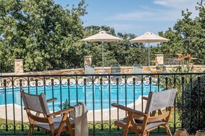 A poolside area with two wooden chairs and two umbrellas, surrounded by a wrought iron fence and lush greenery. - Villa Daphni in Rethymno (Rethymno)