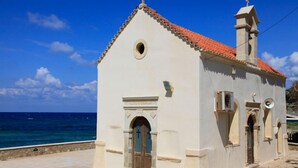 Une petite église avec un toit recouvert de tuiles rouges et une façade blanche, située près d’une étendue d’eau.