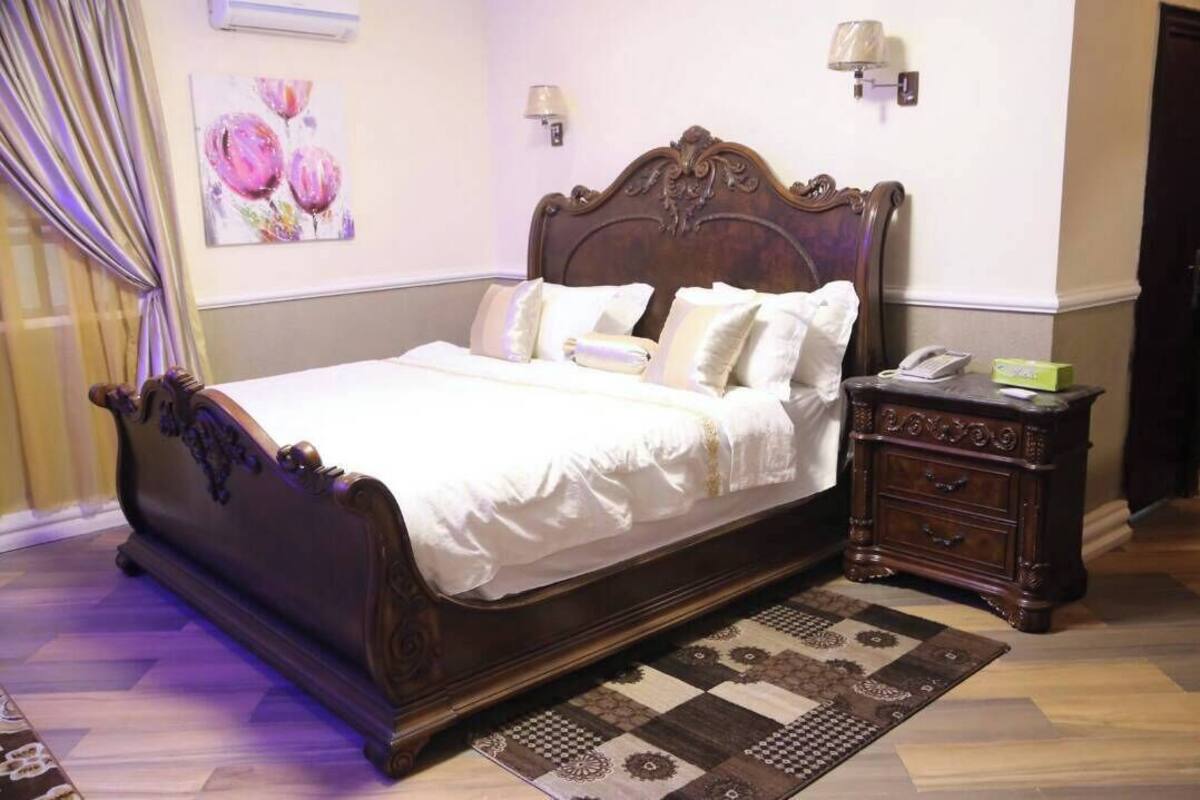 A bedroom with a large bed, a nightstand, a lamp, and a painting on the wall.