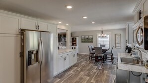 A spacious kitchen with a large refrigerator, a dining area with a chandelier, and a view of the living room. - Serenity On Rice Lake (Brainerd)