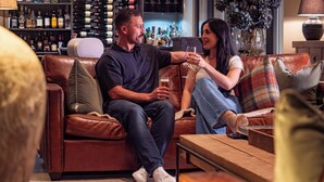 Ein Paar sitzt auf einer Ledersofa, im Hintergrund ist eine Bar zu sehen.