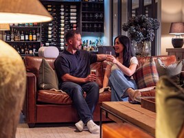 Una pareja sentada en un sofá de cuero, con un bar al fondo.