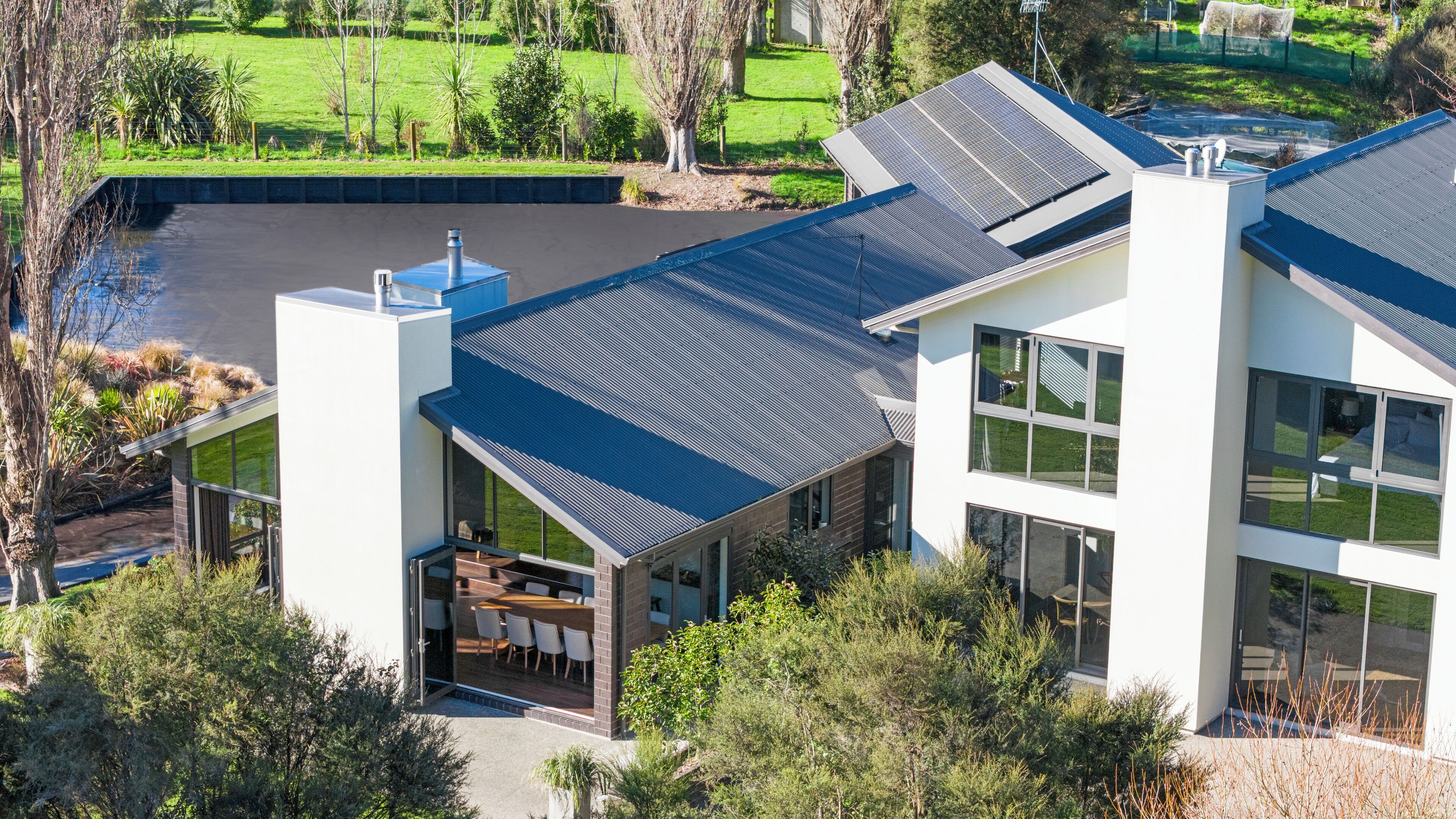A modern house with a large patio, a swimming pool, and a view of a green landscape.