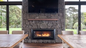 Ein Steinkamin mit einem Fernseher darüber, begleitet von zwei Holztischen und Stühlen.