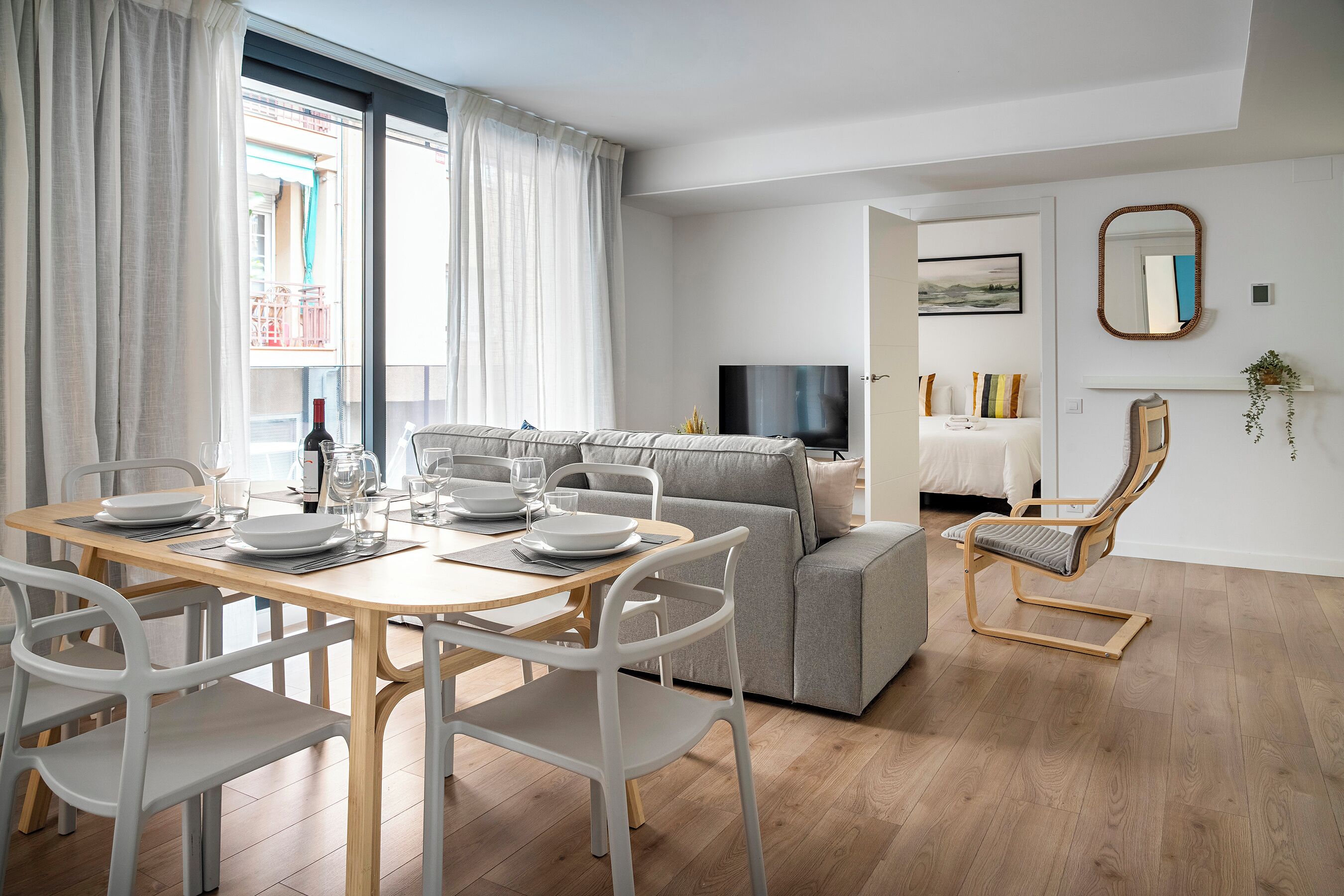 A modern living room with a dining area, a grey sofa, a wooden coffee table, and a TV.