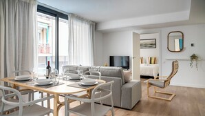 A modern living room with a dining area, a grey sofa, a wooden coffee table, and a TV. - Habitat Apartments Teatre (L'Hospitalet de Llobregat)