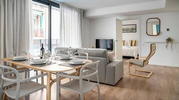 A modern living room with a dining area, a grey sofa, a wooden coffee table, and a TV.