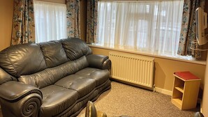Ein Wohnzimmer mit einer Ledersofa, einem Heizkörper, einem Holztisch und blumigen Vorhängen.
