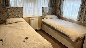 Ein Hotelzimmer mit zwei Einzelbetten, einem Heizkörper und blumigen Vorhängen.