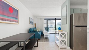 Eine moderne Küche mit einem Edelstahlkühlschrank, einem Esstisch mit Bänken, einem blauen Sofa und einem Balkon mit Aussicht.