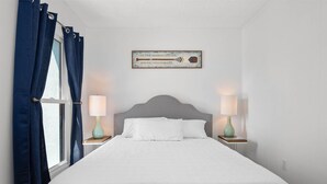 Ein ordentlich bezogenes Bett mit grauem Kopfteil, zwei Nachttischlampen und einem gerahmten Schild an der Wand.