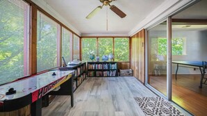 Una habitación con un ventanal grande, un ventilador de techo, una estantería y una mesa.