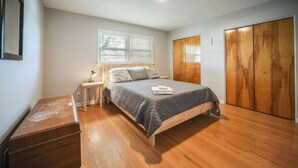 Un dormitorio con cama de madera, una mesita de noche con lámpara, un escritorio de madera y un armario.