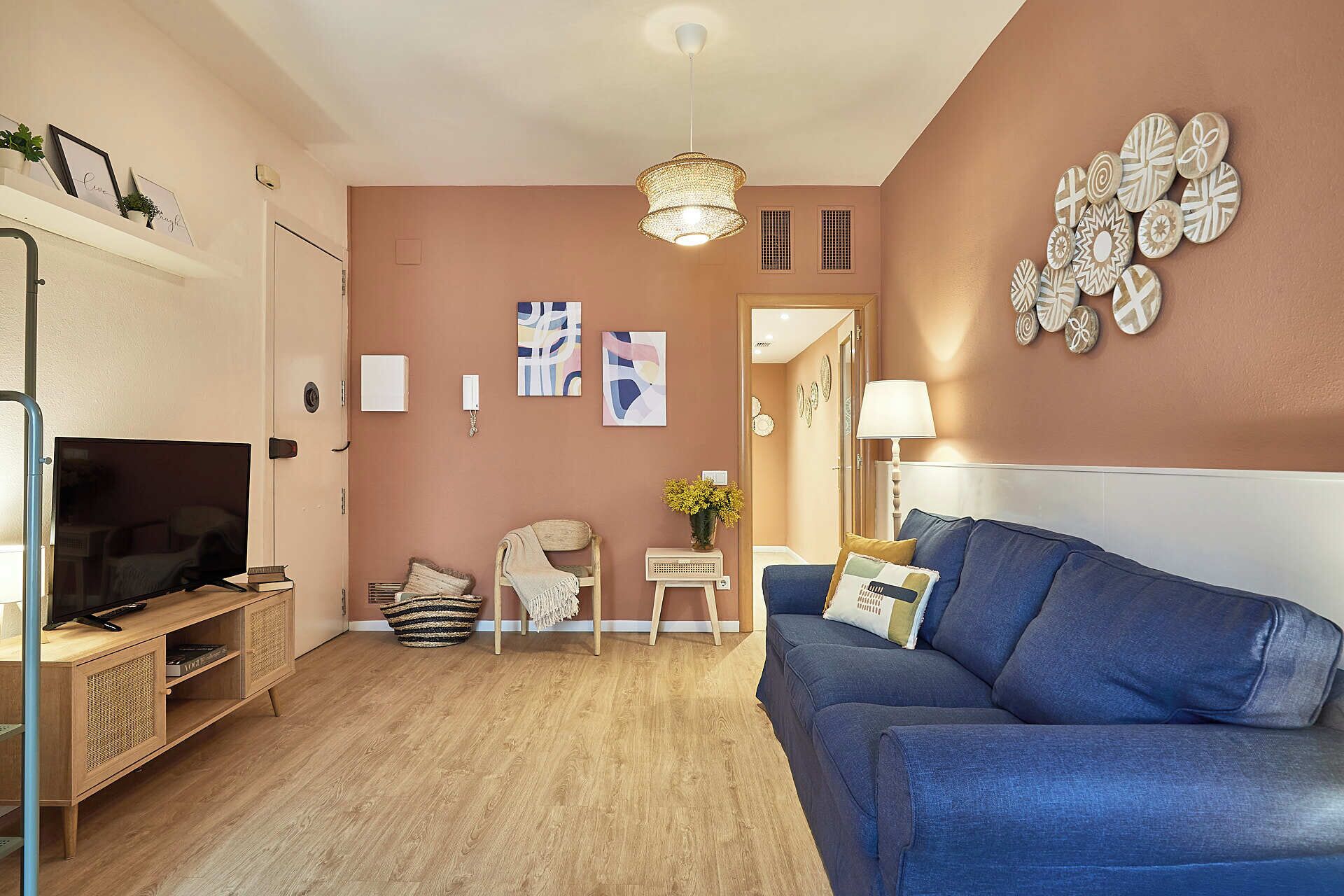 Un salon avec un canapé bleu, un téléviseur, un mur décoratif et une petite table sur laquelle est posé un vase.