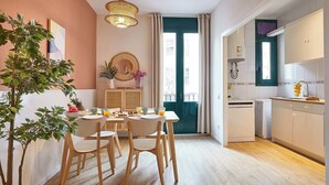 Eine moderne Küche mit Essbereich, ausgestattet mit einem Holztisch und Stühlen, einer Hängeleuchte und Blick durch eine grüne Tür.
