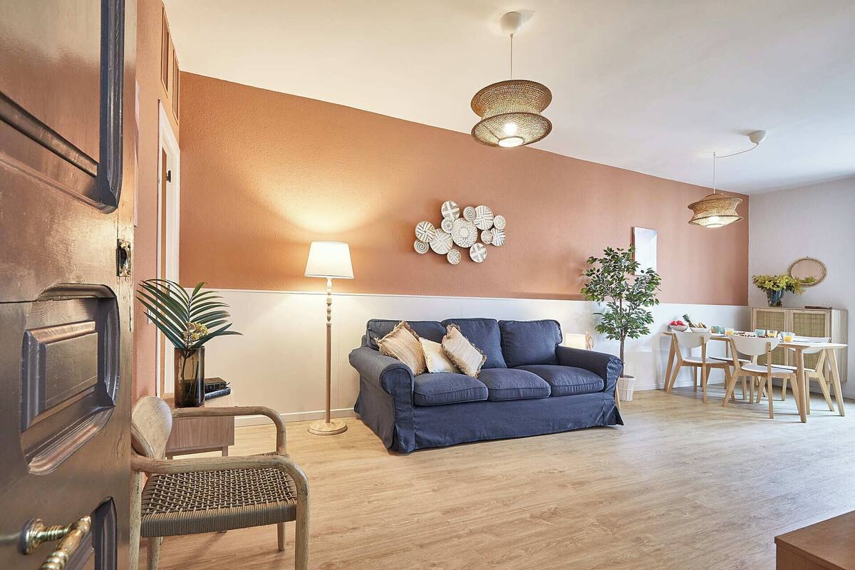 Ett modernt vardagsrum med en blå soffa, en golvlampa och en matplats med ett bord och stolar.