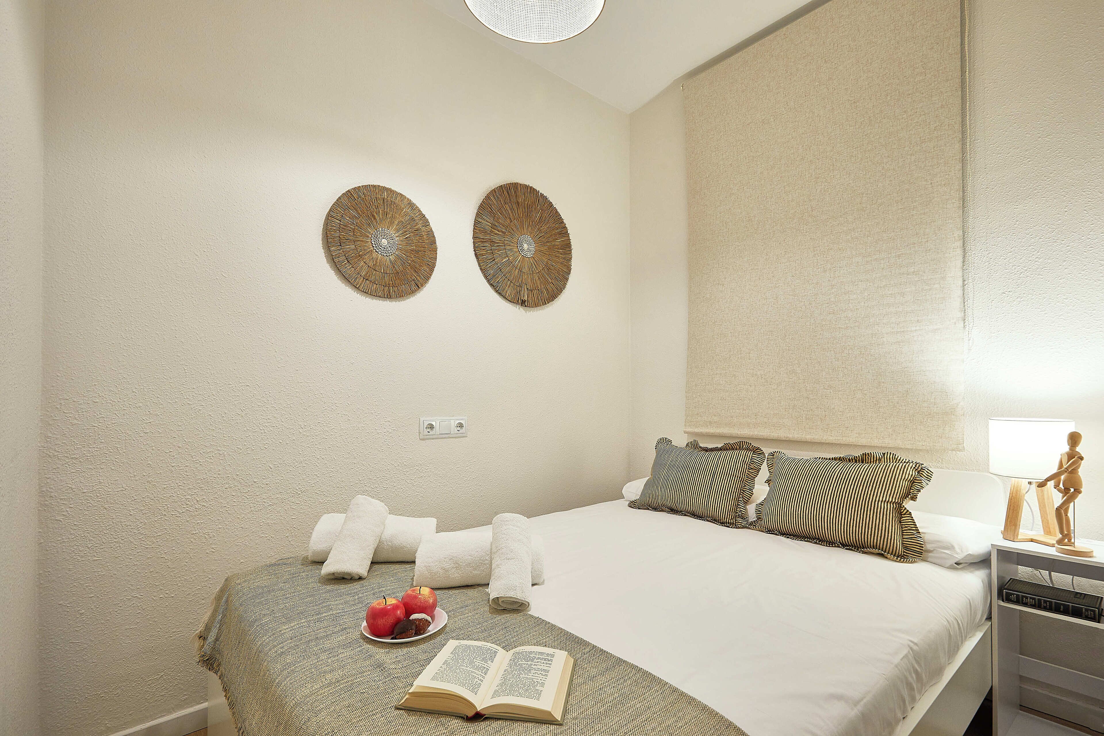 A neatly made bed with a green blanket, two decorative wall pieces, and a bedside table with a lamp and a small statue.