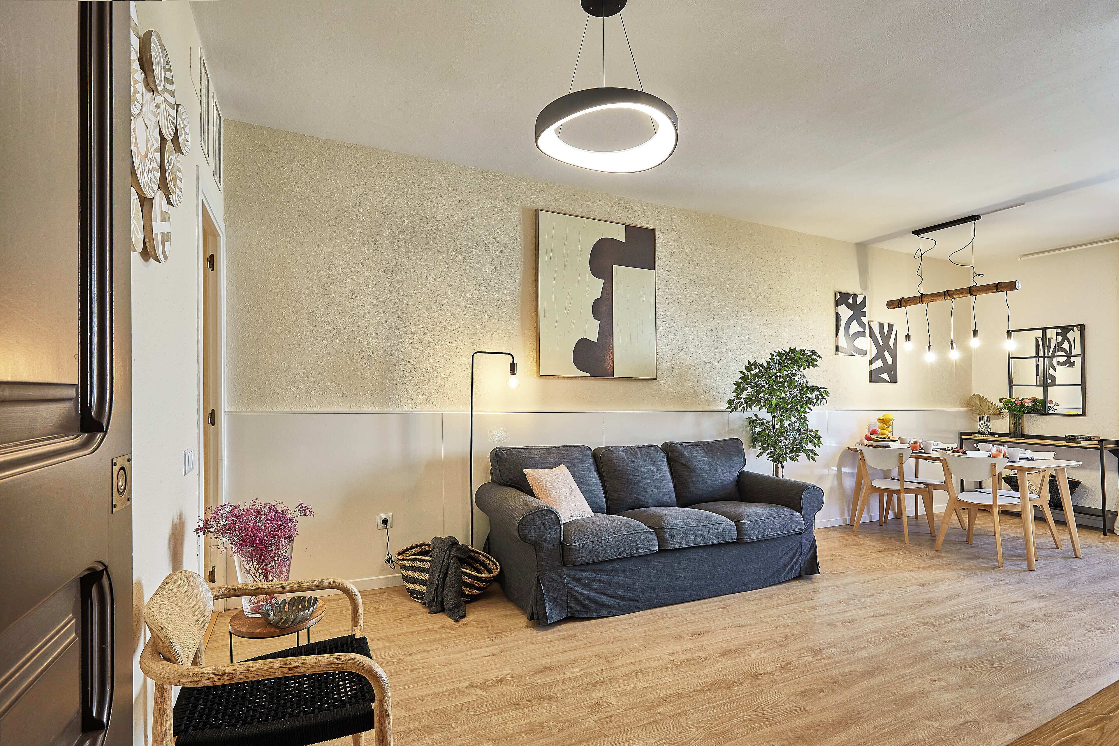 A modern living room with a grey sofa, wooden floor, and a dining area with a table and chairs.