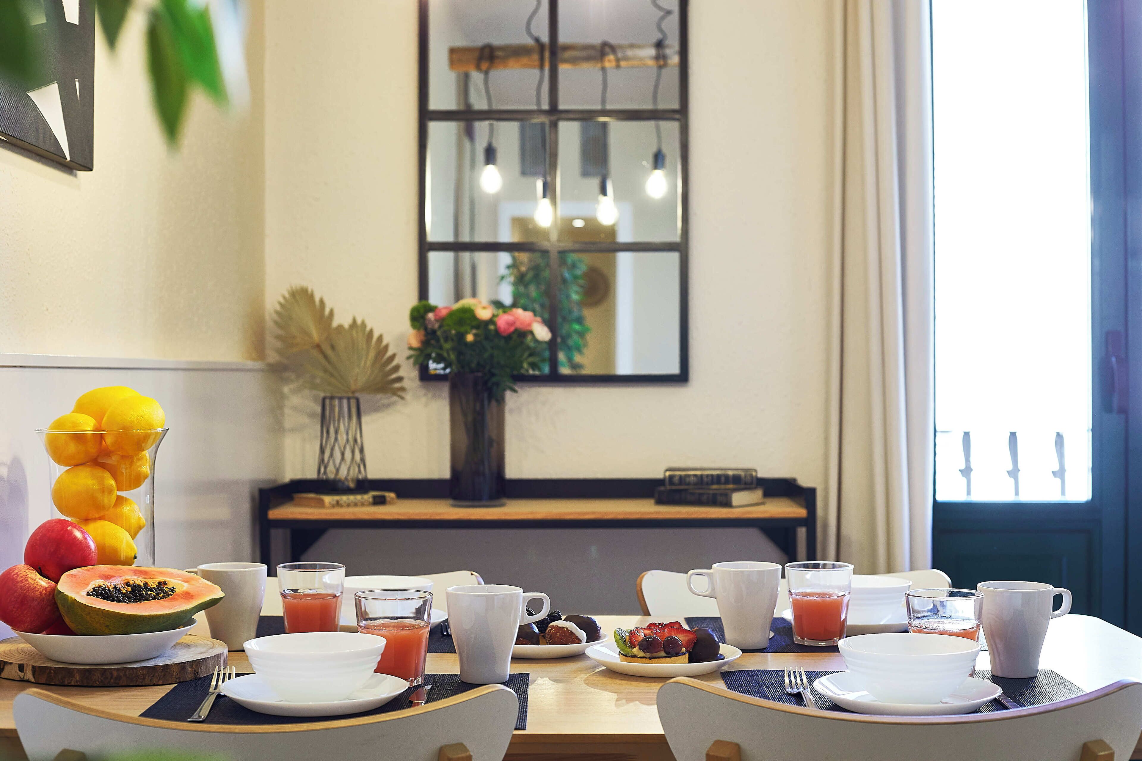 Une table mise pour le petit-déjeuner, avec des fruits, des jus de fruits et des tasses de café.