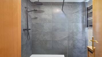 A shower with a handheld showerhead and a wall-mounted head, tiled with grey stone.