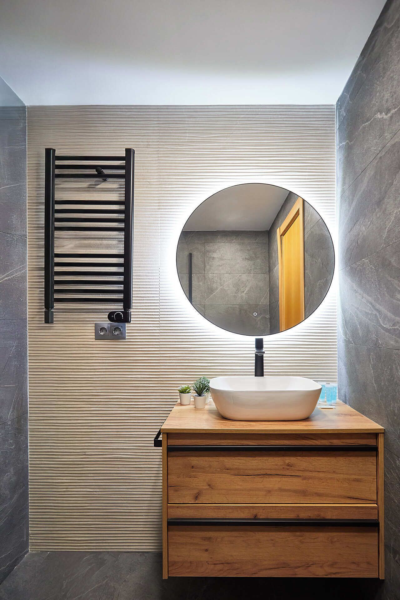 A modern bathroom with a wooden vanity, a round mirror, and a towel rack.