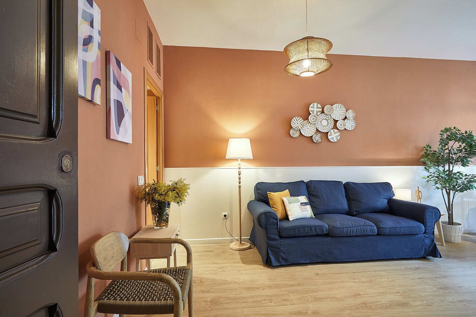 A living room with a blue sofa, a wooden chair, a floor lamp, and a wall with decorative plates.